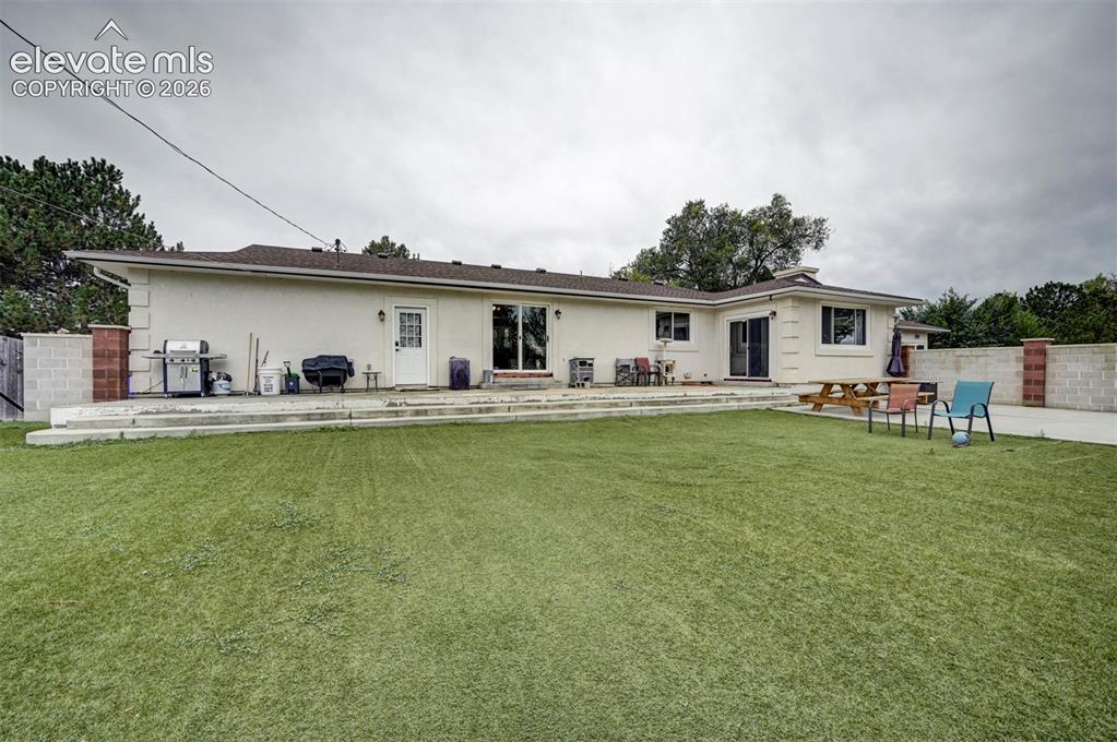 Image 42 of 50: Expansive artificial turf lawn with a multi-level concrete patio, stucco ex