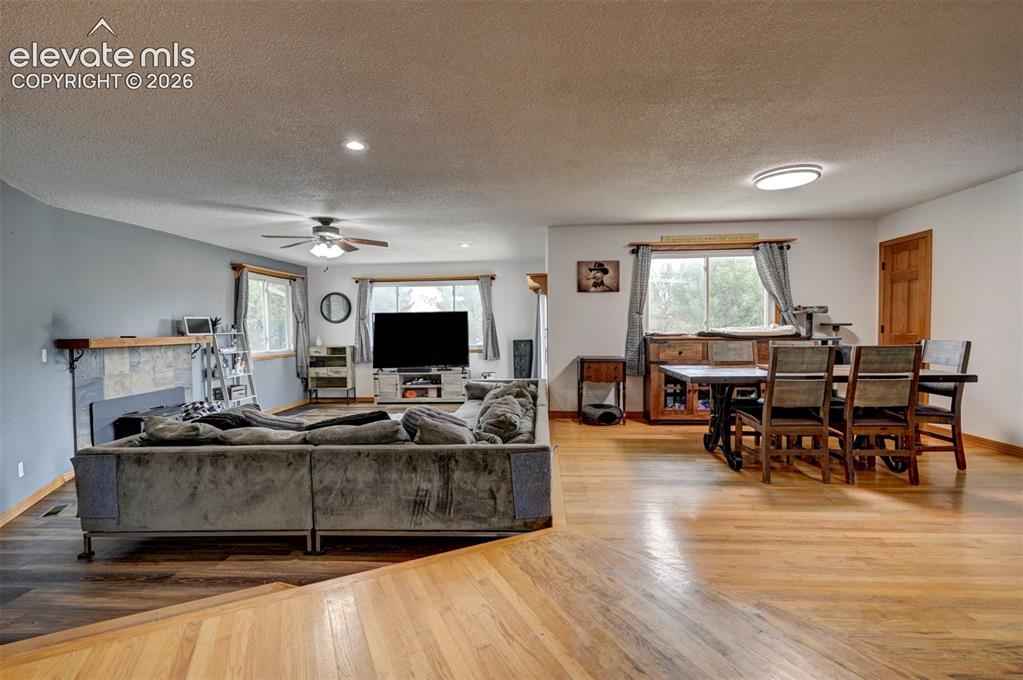 Image 5 of 50: Open-concept living space featuring wood-finish flooring, a stone-clad fire