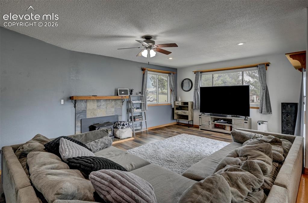 Image 7 of 50: Living area featuring wood-finish flooring, a ceiling fan, and a stone-surr