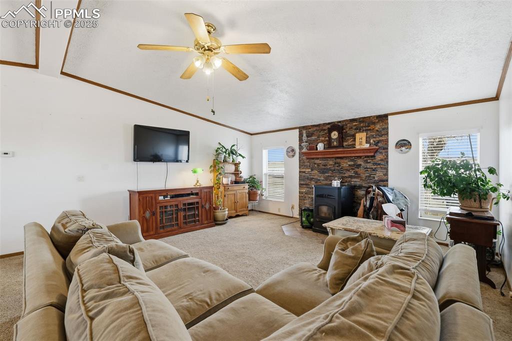 Image 12 of 49: Carpeted living room featuring a wood stove, crown molding, a textured ceil