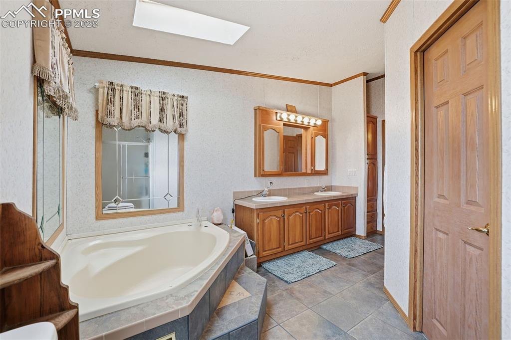 Image 22 of 49: Full bathroom with ornamental molding, a bath, double vanity, a skylight, a