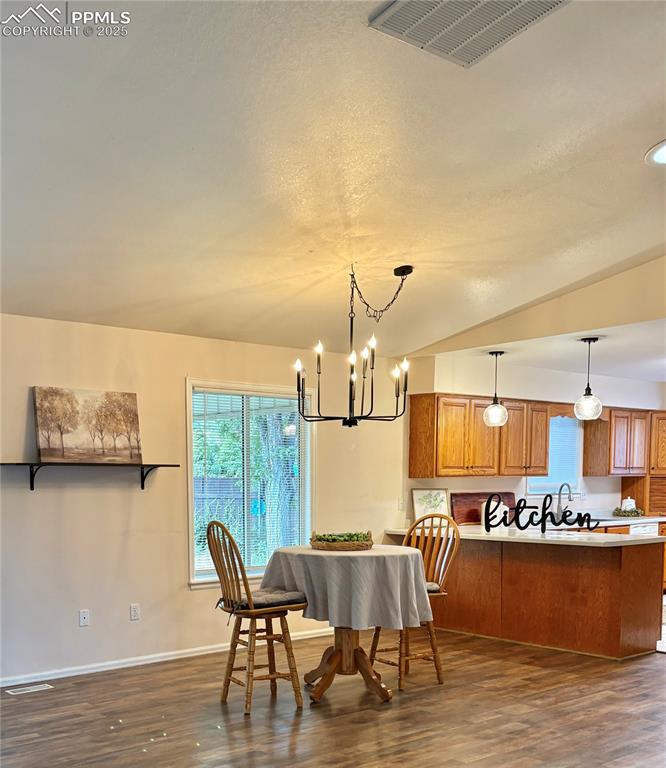 Image 12 of 27: Dining area featuring dark wood-type flooring, a chandelier, and vaulted ce