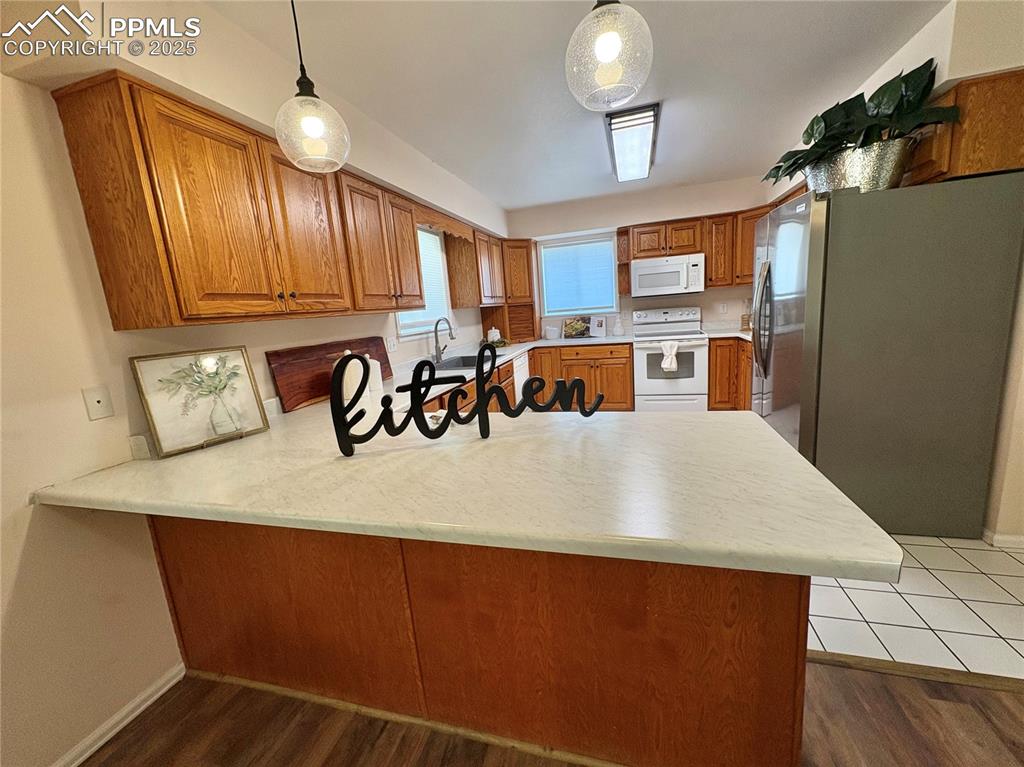 Image 13 of 27: Kitchen with a peninsula, brown cabinets, light countertops, and pendant li
