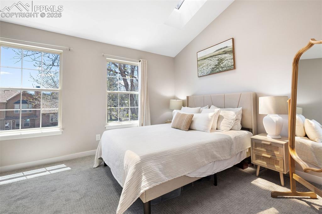 Image 14 of 26: Bedroom featuring vaulted ceilings with a skylight, two large windows, soft