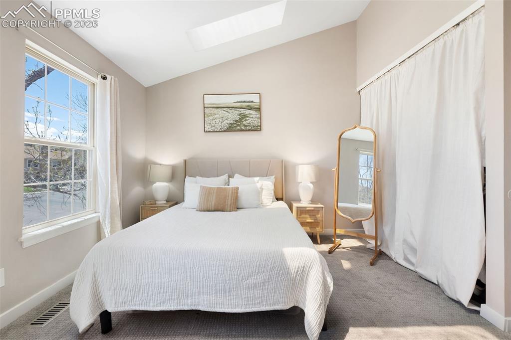 Image 16 of 26: Vaulted ceiling bedroom with a skylight and a large double-hung window