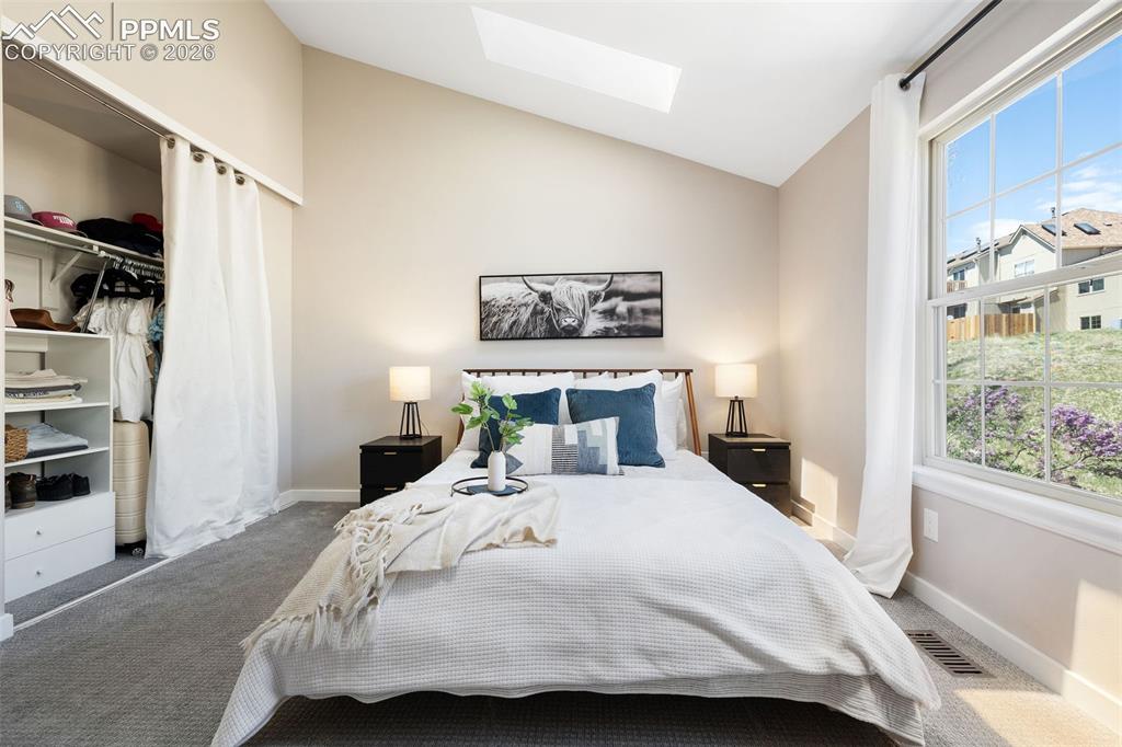 Image 21 of 26: Vaulted ceiling bedroom with a large window, skylight, and wall-to-wall car
