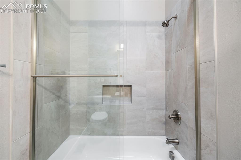 Image 24 of 26: Bathtub with a glass shower enclosure and brushed nickel fixtures