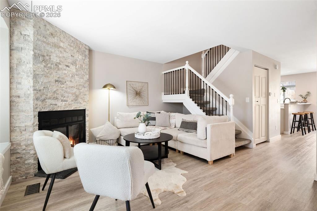 Image 4 of 26: Living area featuring a stone-clad fireplace, wood-finish flooring, and a s
