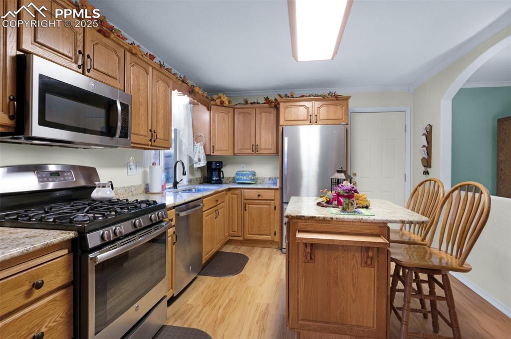 Image 9 of 31: Kitchen featuring a kitchen island, a sink, arched walkways, light wood-sty