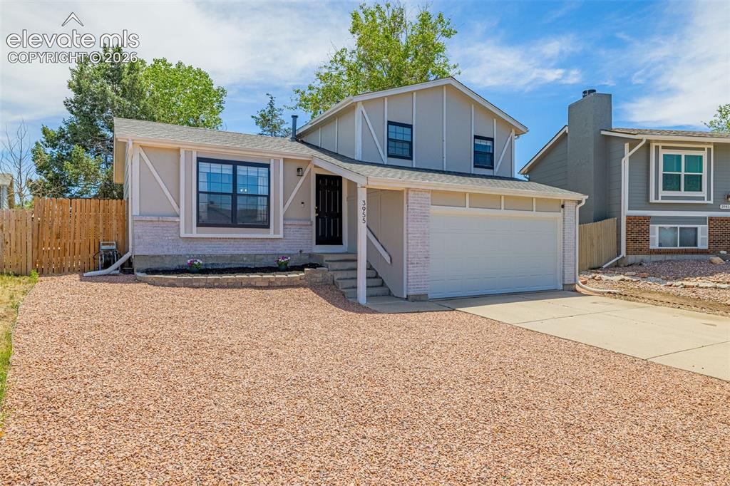 Image 2 of 29: Split-level residence featuring a two-car garage, gravel front yard, white