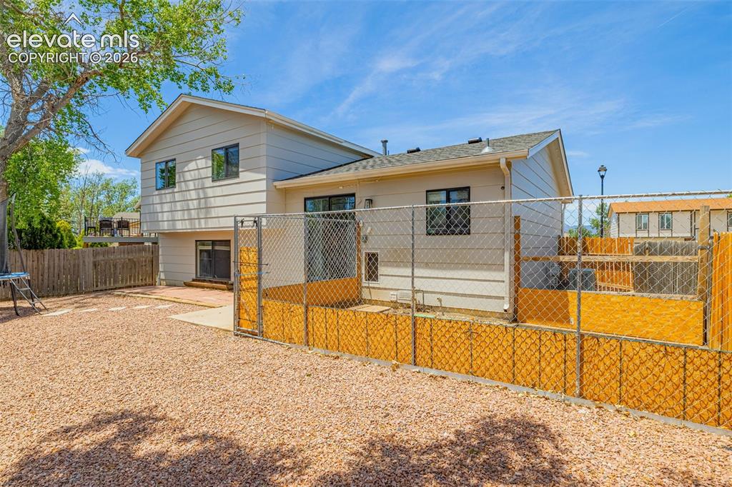Image 21 of 29: Rear exterior featuring neutral siding, a gravel yard, a partial wood fence