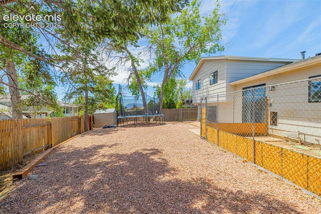 Image 23 of 29: Spacious backyard featuring gravel landscaping, mature trees, a privacy fen