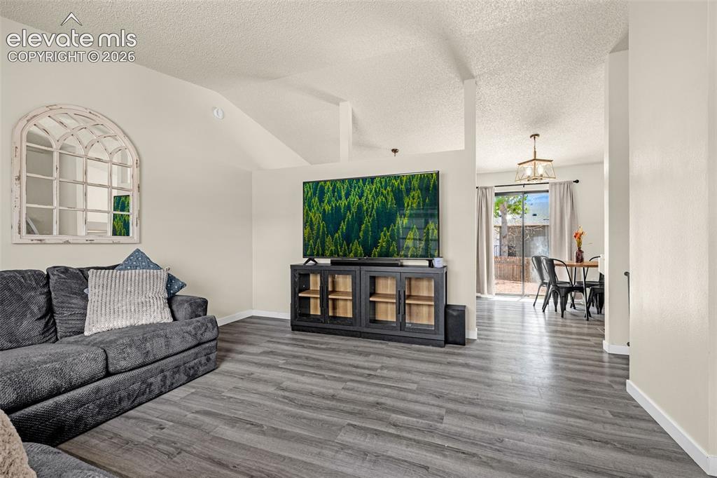 Image 5 of 29: Spacious living area featuring wood-finish flooring, vaulted ceilings, and