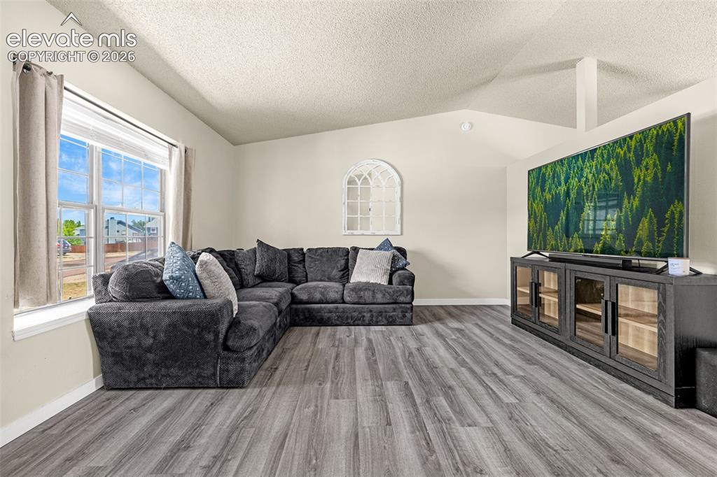 Image 6 of 29: Spacious living area featuring wood-finish flooring, a large window with wh