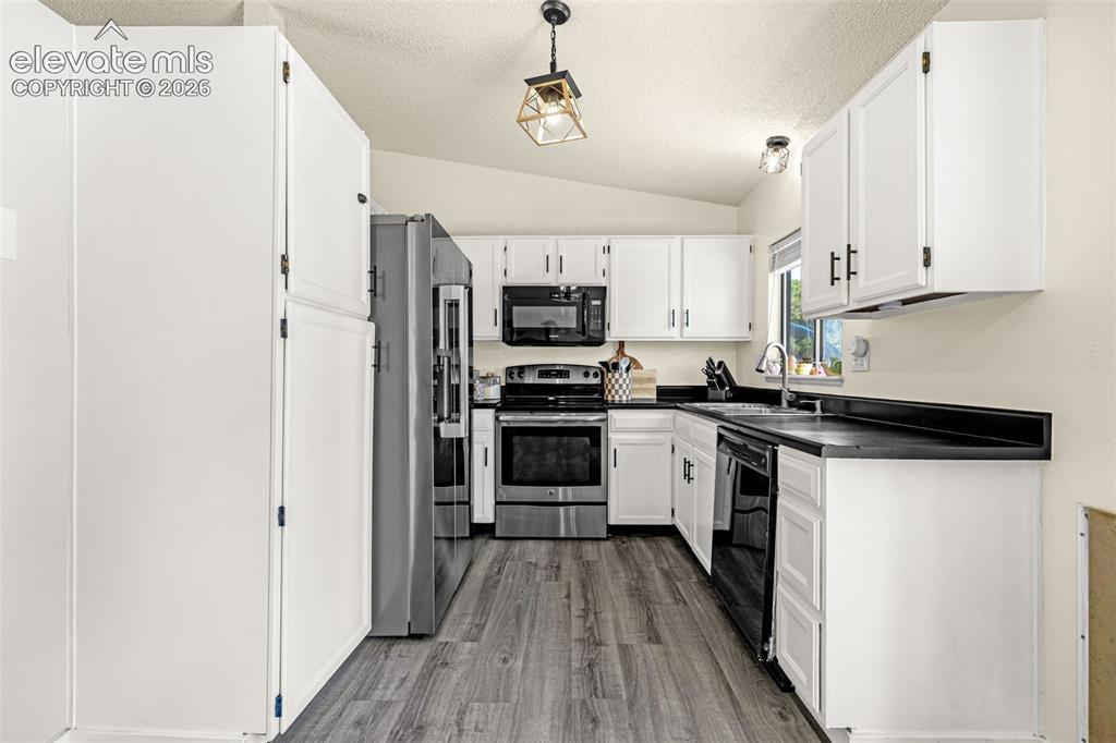 Image 8 of 29: Modern kitchen featuring white cabinetry with black hardware, dark countert