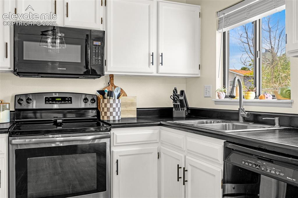 Image 9 of 29: Kitchen featuring white cabinetry with black hardware, black countertops, s