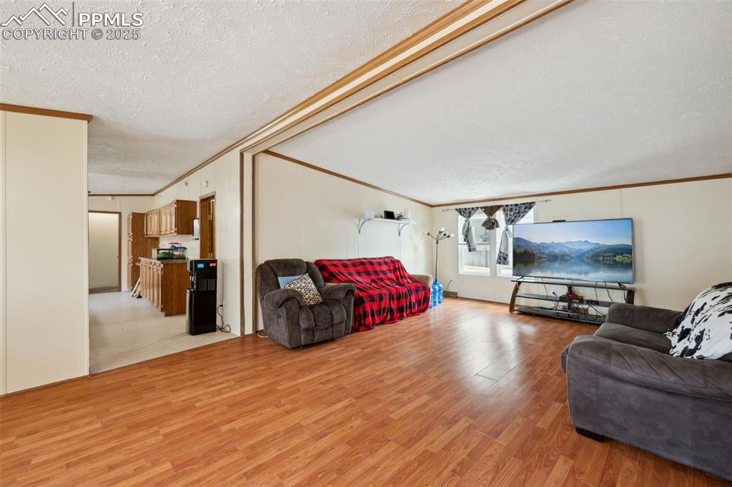 Image 15 of 34: Living area with a textured ceiling, crown molding, and light wood-style fl