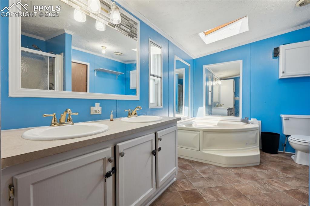 Image 27 of 34: Full bathroom with a skylight, crown molding, double vanity, a bath, and to
