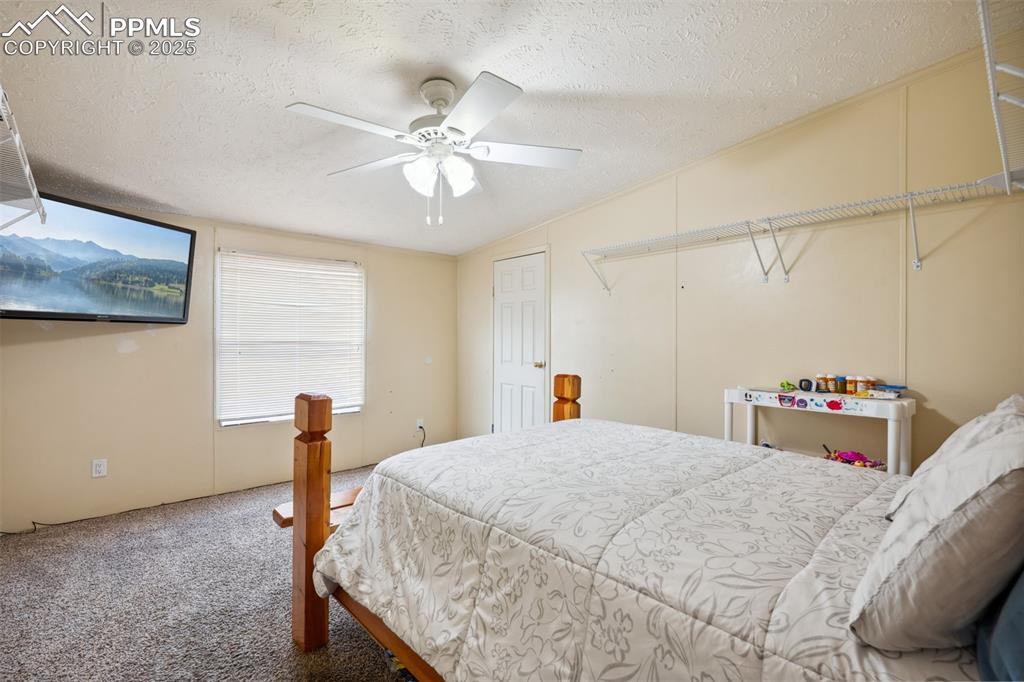 Image 32 of 34: Bedroom with a textured ceiling, carpet flooring, ceiling fan, and attic ac