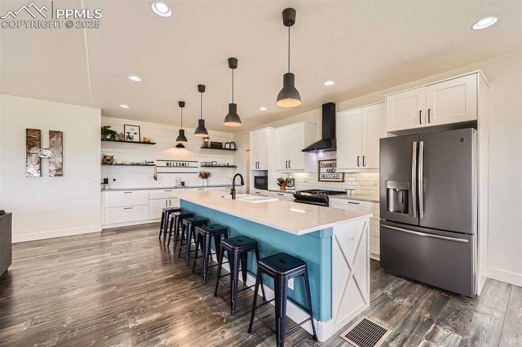 Image 10 of 29: Kitchen featuring stainless steel fridge, open shelves, white cabinets, lig