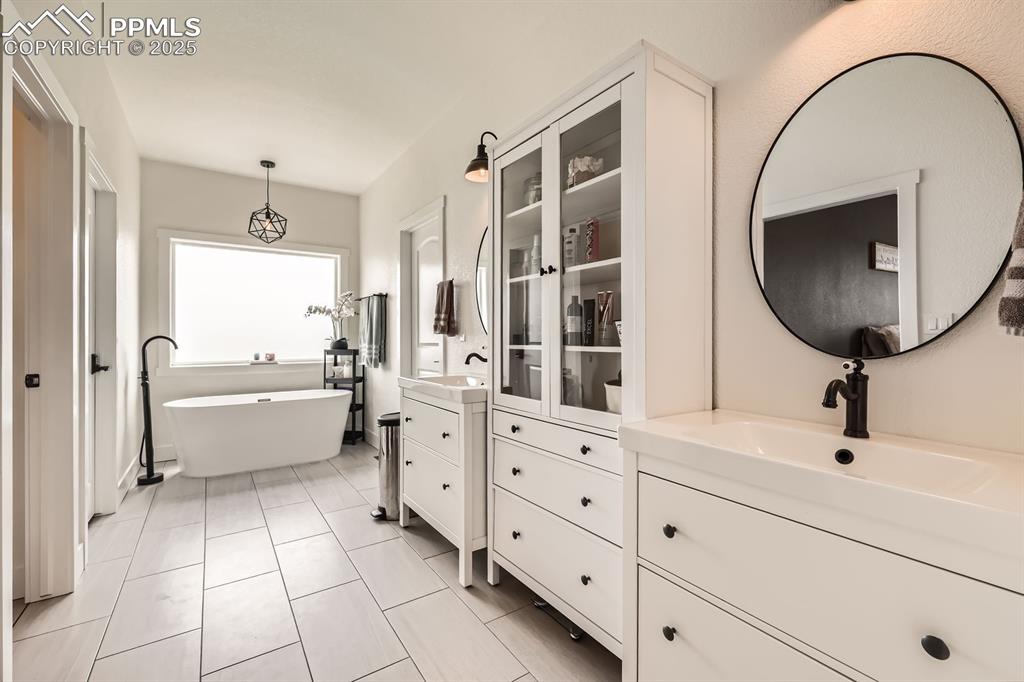 Image 16 of 29: Full bathroom with two vanities, a freestanding tub, and tile patterned flo