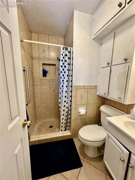 Image 14 of 20: Bathroom featuring tile patterned flooring, a stall shower, a textured ceil