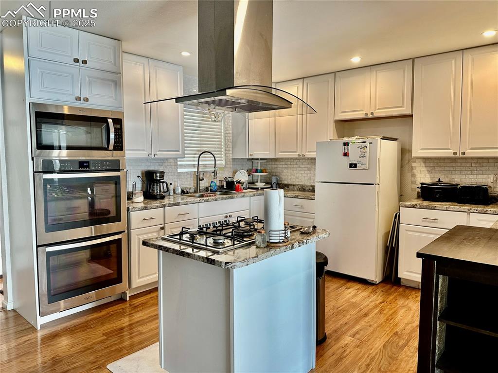 Image 6 of 20: Kitchen with stainless steel appliances, island range hood, decorative back