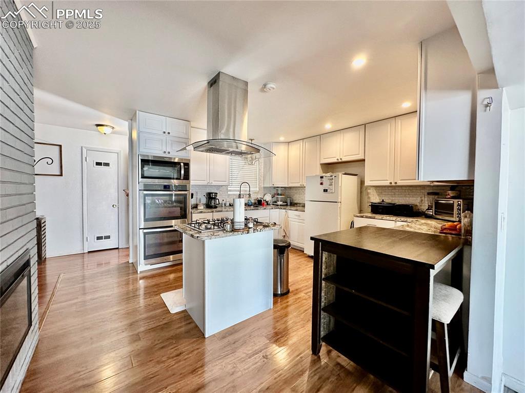Image 7 of 20: Kitchen featuring island range hood, stainless steel appliances, backsplash