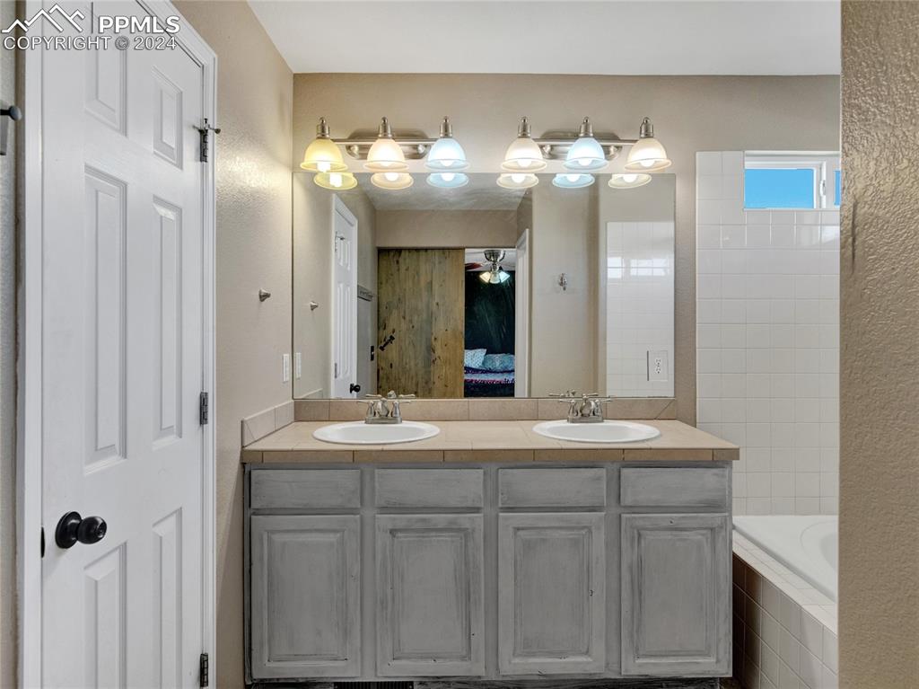 Image 17 of 23: Bathroom with ceiling fan, tiled tub, and vanity