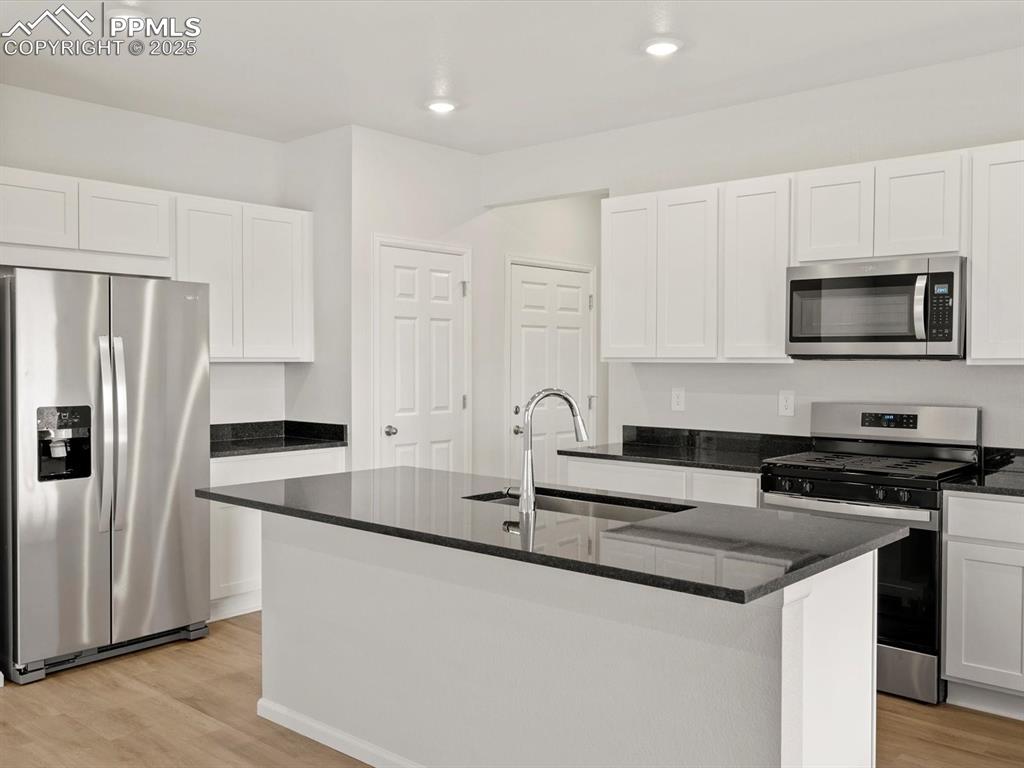 Image 3 of 23: Kitchen with appliances with stainless steel finishes, white cabinets, ligh