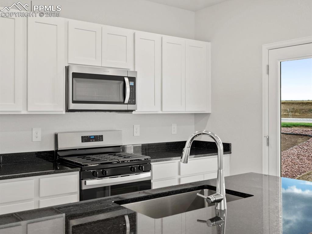 Image 4 of 23: Kitchen featuring stainless steel appliances, dark stone countertops, and w