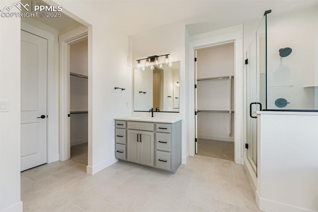 Image 14 of 27: Bathroom with a walk in closet, a shower stall, vanity, and light tile patt