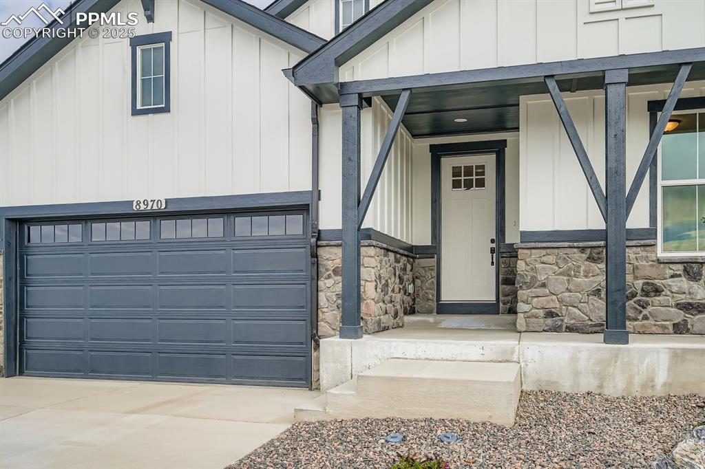Image 4 of 27: View of exterior entry with board and batten siding, a garage, a porch, dri
