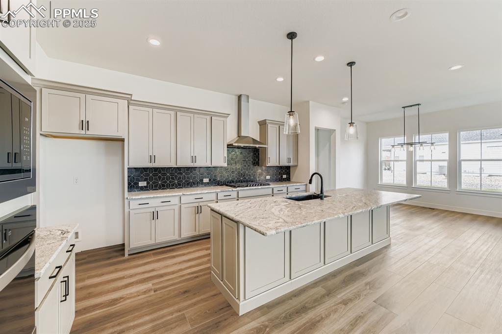 Image 8 of 27: Kitchen featuring backsplash, oven, light stone countertops, hanging light