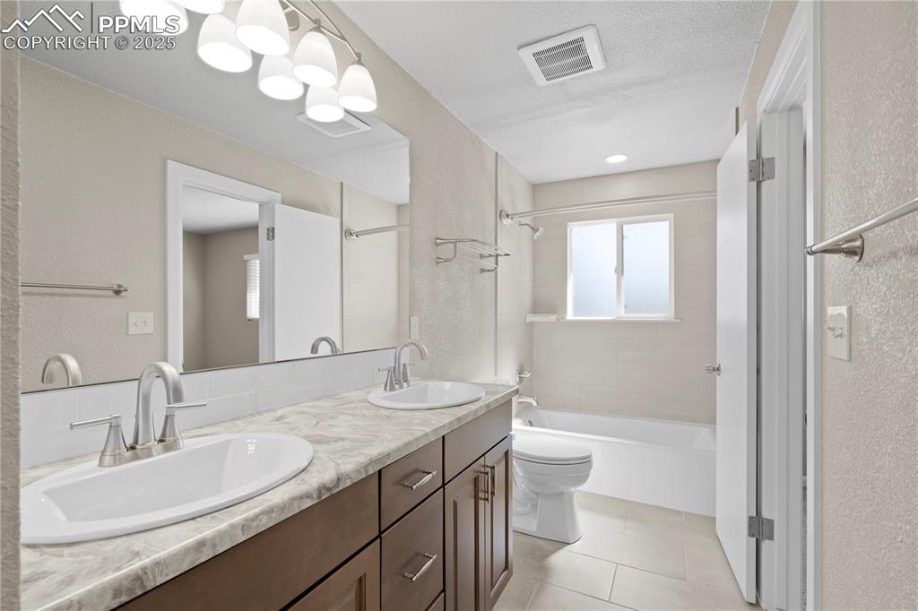 Image 6 of 35: Full bathroom with a textured wall, double vanity, washtub / shower combina