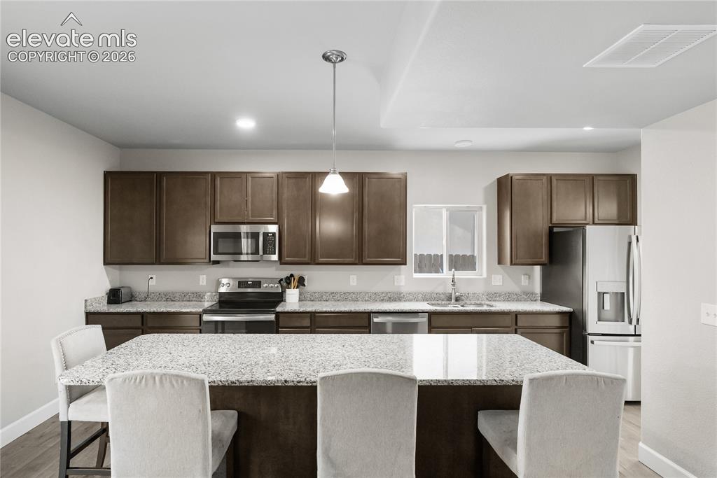 Image 12 of 42: Kitchen featuring dark wood cabinetry, light-toned stone-finish countertops