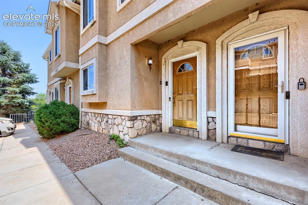 Caption: Stucco exterior with stone accent, concrete entryway, and mature landscaping