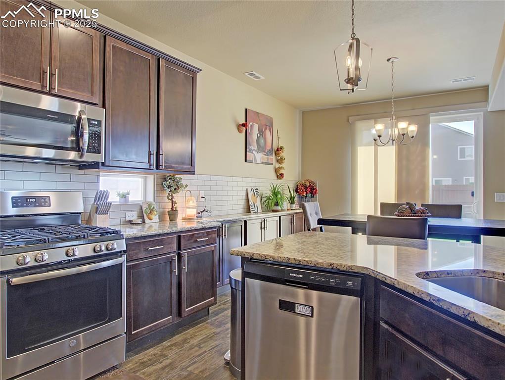 Image 11 of 30: Kitchen featuring dark brown cabinetry, stainless steel appliances, pendant