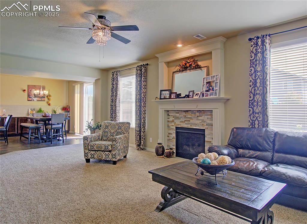 Image 14 of 30: Carpeted living area featuring a fireplace, ceiling fan, and a chandelier