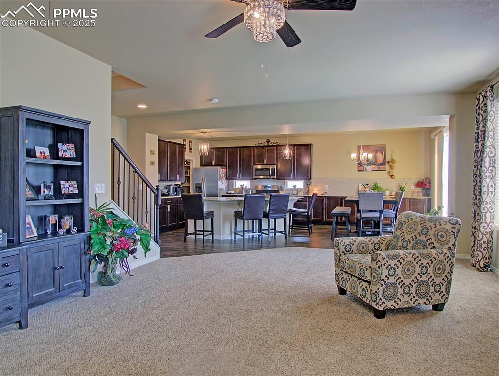 Image 15 of 30: Living room with light carpet, a chandelier, and a ceiling fan