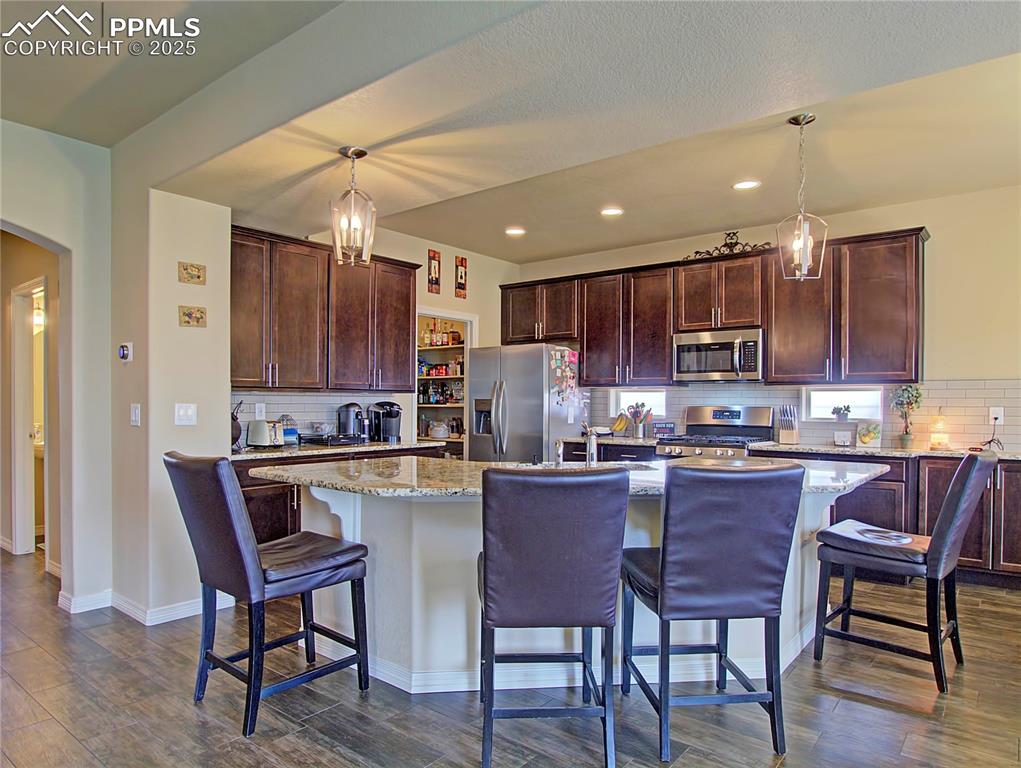 Image 7 of 30: Kitchen featuring backsplash, a breakfast bar, a chandelier, light stone co