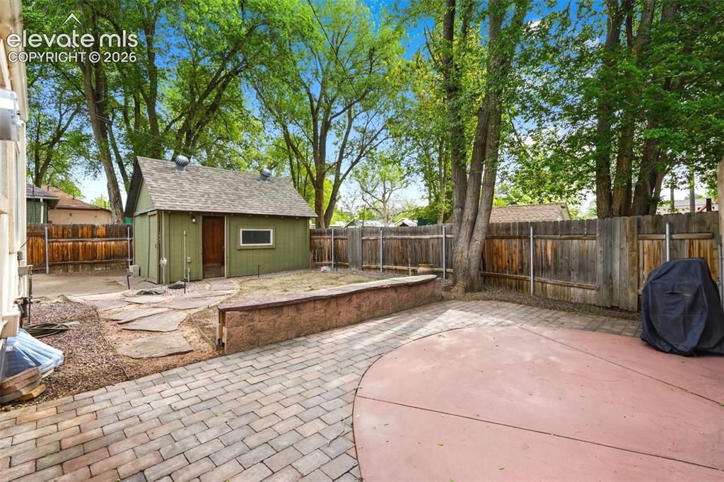 Image 28 of 40: Expansive backyard featuring a detached green storage shed with a gabled ro