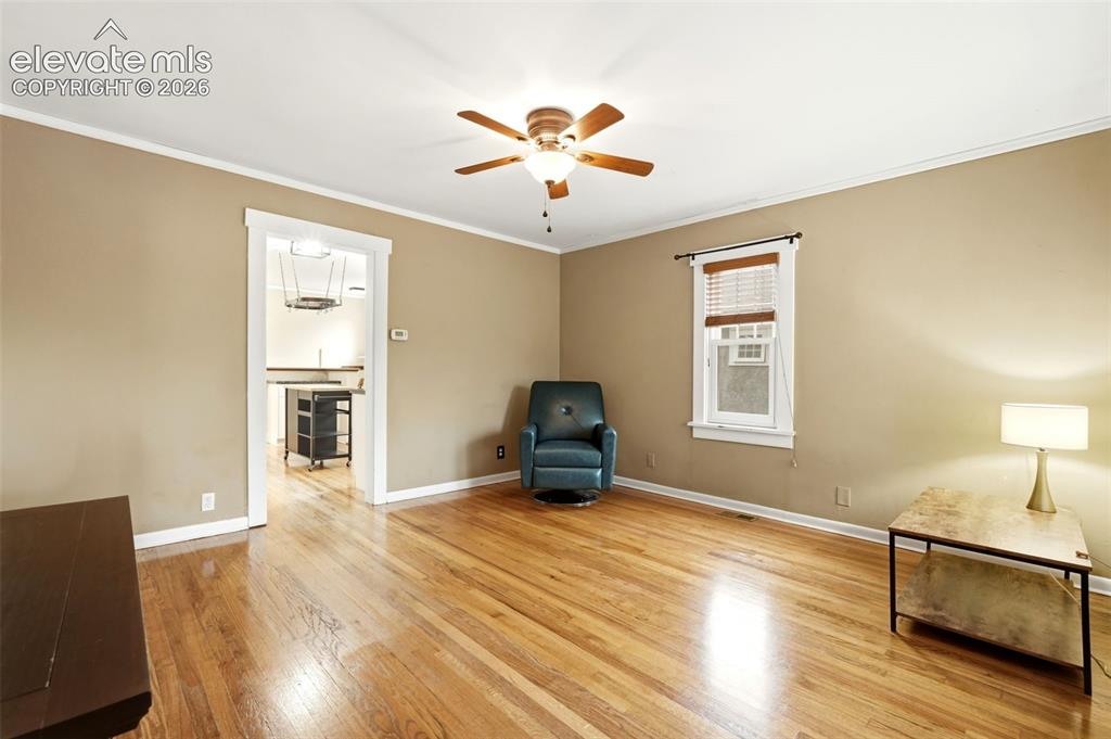 Image 5 of 40: Hardwood flooring throughout the room, crown molding, ceiling fan, and trim