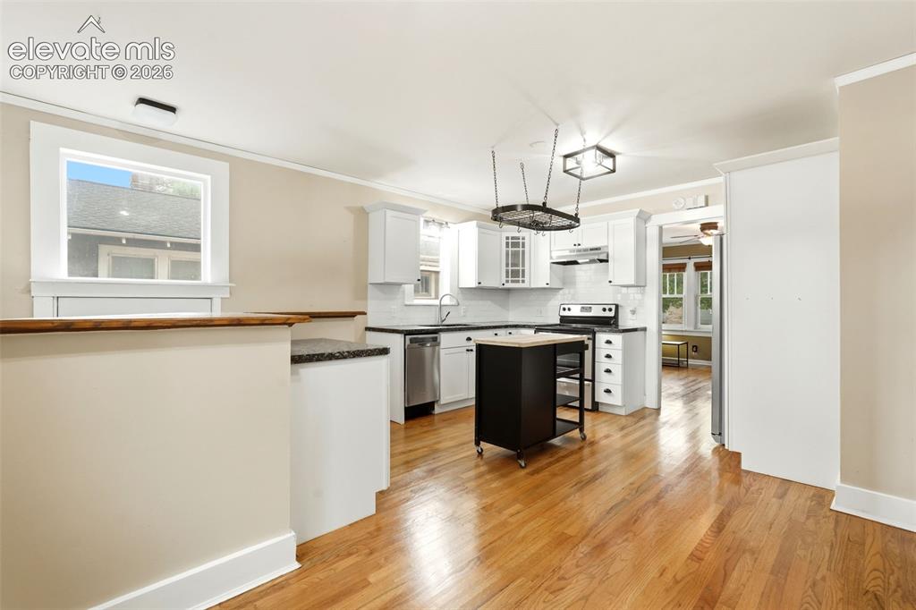Image 9 of 40: Open-concept kitchen featuring wood flooring, white cabinetry, dark counter