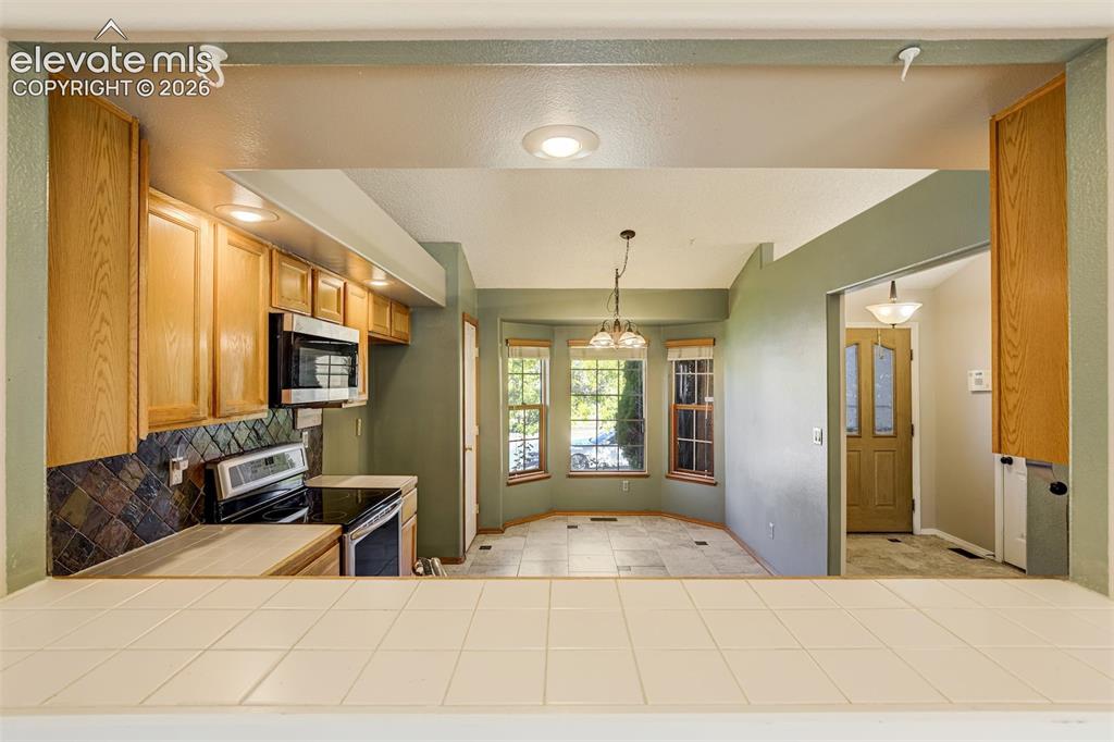 Image 13 of 50: Kitchen pass-through with tiled countertop, wood cabinetry, and stainless s