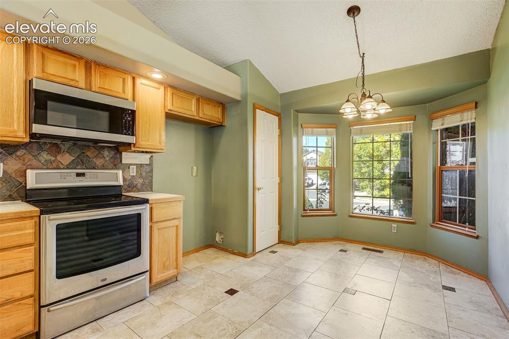 Image 15 of 50: Kitchen with light wood cabinetry, stainless steel appliances, and a tiled