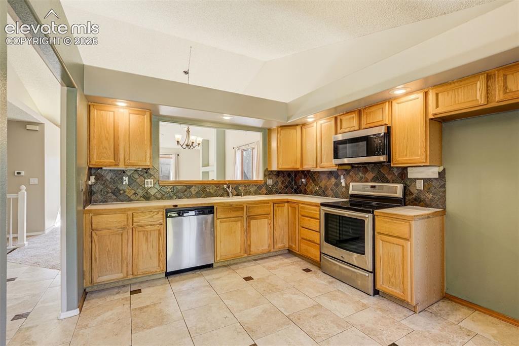 Image 19 of 50: Kitchen featuring wood cabinetry, stainless steel appliances, tile flooring