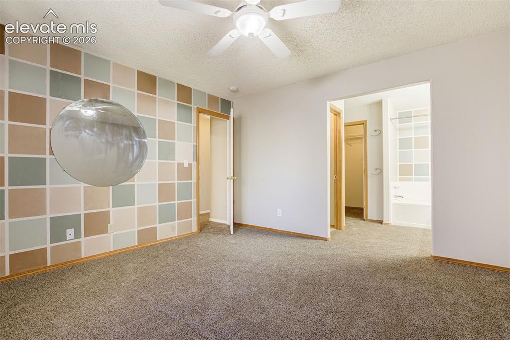 Image 24 of 50: Carpeted room featuring a ceiling fan, a patterned accent wall, and a doorw