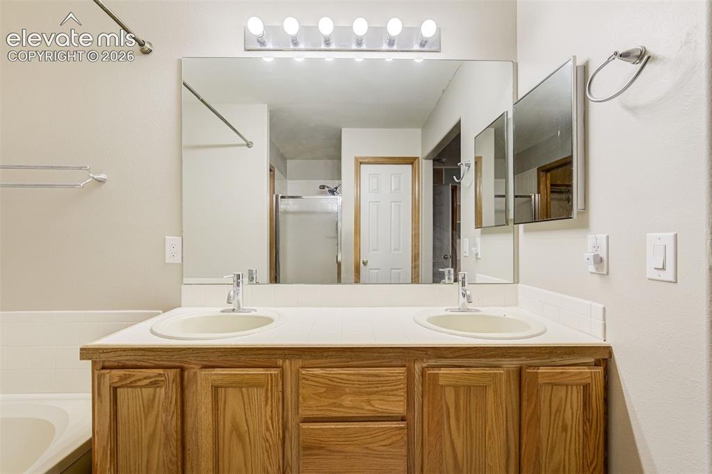 Image 26 of 50: Wood-finish vanity with dual integrated sinks, chrome fixtures, and a large
