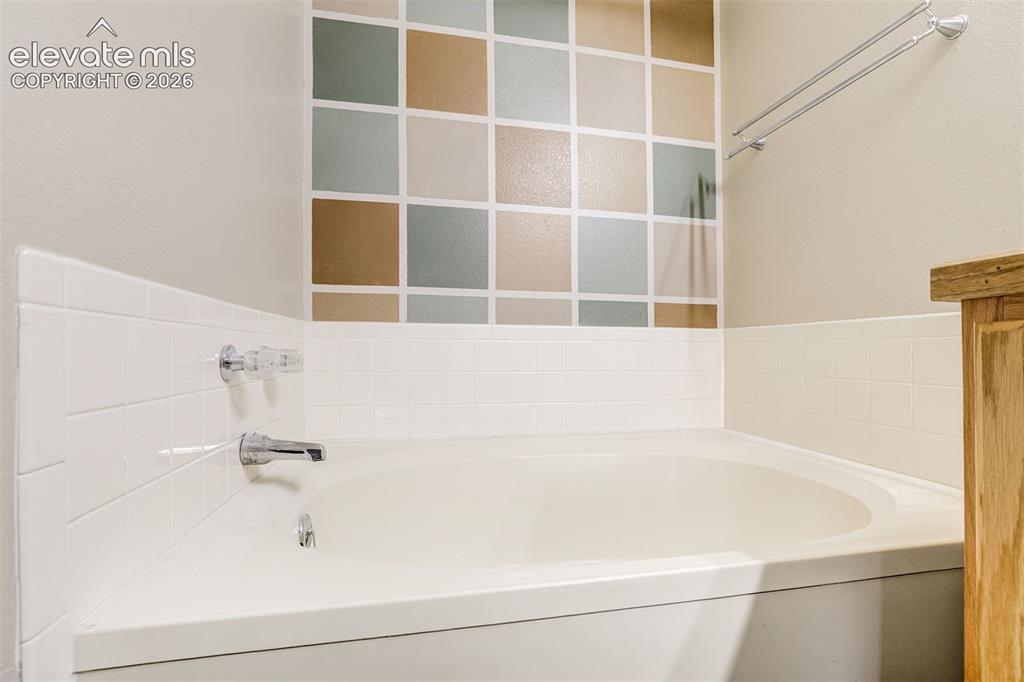 Image 28 of 50: Built-in tub with chrome fixtures, white subway tile surround, and an accen
